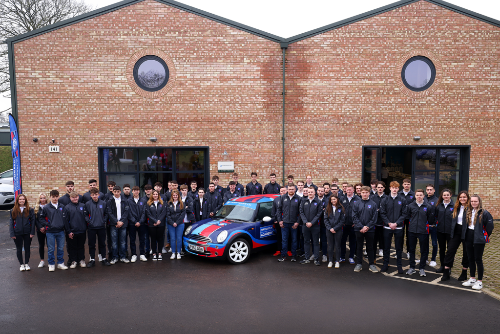 2023 Motorsport UK Academy drivers standing outside the Motorsport UK HQ beside a Mini Cooper with Union Jack design